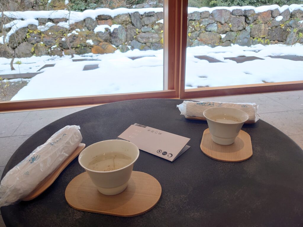 星のや京都の舟待合室にて提供された薬草湯とおしぼり。雪景色を背景にした和モダンなテーブルセッティング。