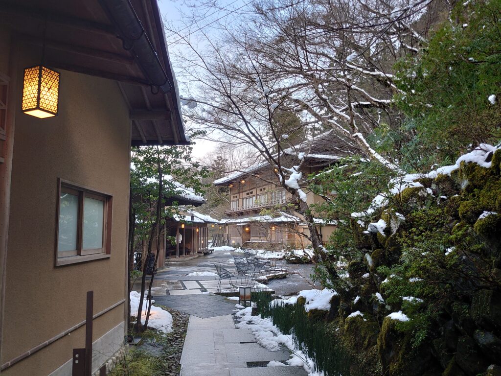 星のや京都の雪景色に囲まれた中庭と客室棟の様子。石畳と照明が和の趣を演出している。