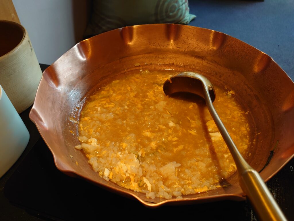 食後に雑炊として仕上げられた鍋の中身。卵とごはんが溶け込んだ優しい色合いの雑炊が銅鍋の中に広がっている。