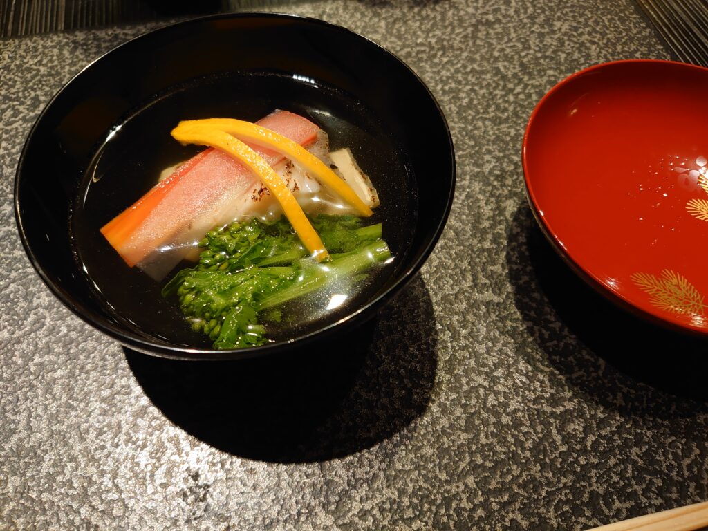 甘鯛と菜の花のお吸い物。黒塗りの椀に彩り鮮やかな具材が映える、上品な一品。
