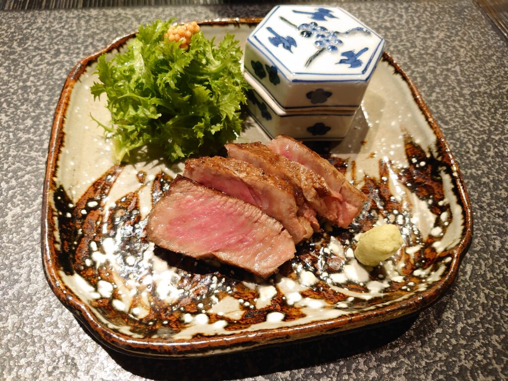 焼物は和牛のグリル。霜降りの焼きたて肉が皿に盛られ、葉わさびが添えられている。